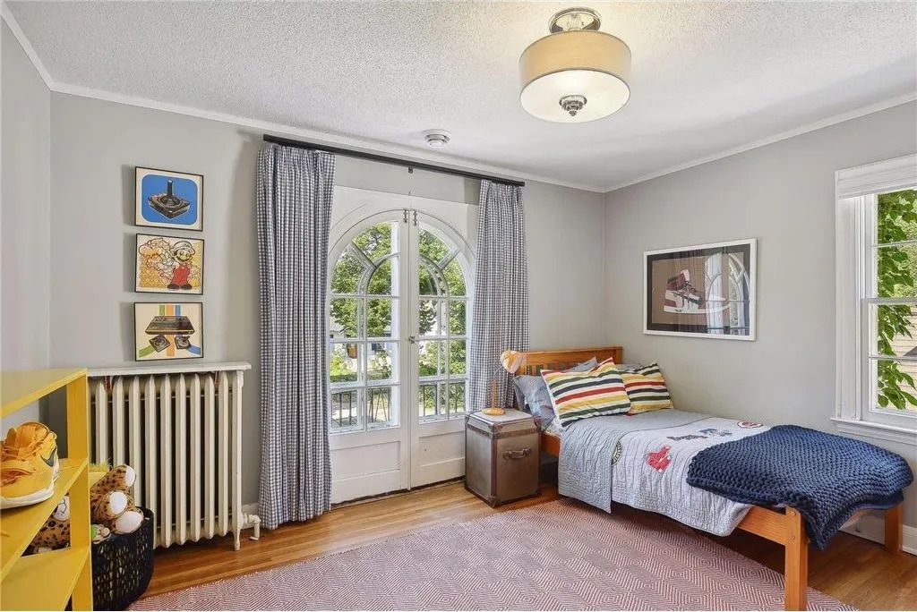 A bedroom with light walls, hardwood floors, a single bed, a radiator, and arched glass doors leading to the outside.