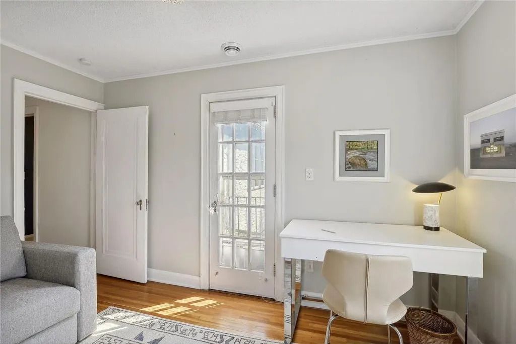 A home office with a grey sofa, a white desk, a tan chair, and a French door leading to the outdoors.