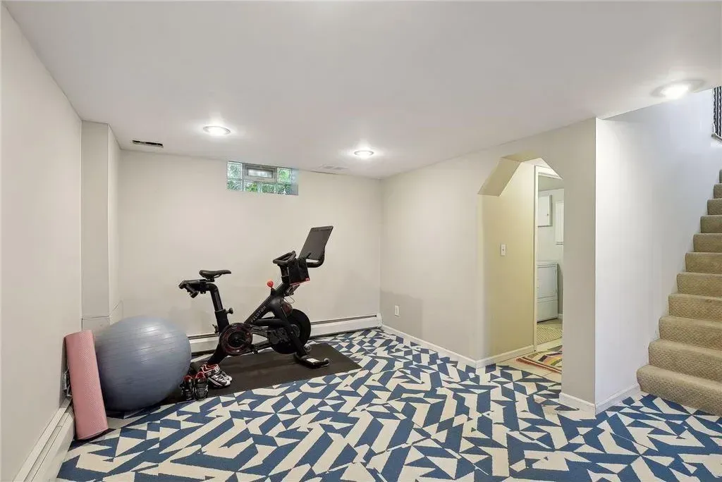 A home gym in a carpeted basement featuring a stationary bike, a blue yoga ball, and a yoga mat, next to carpeted stairs.