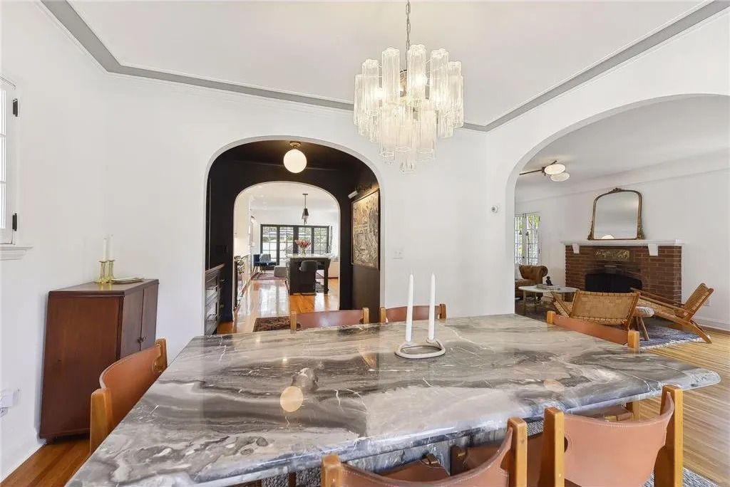A marble dining table in a bright room with an arched doorway leading to a living area with a fireplace.