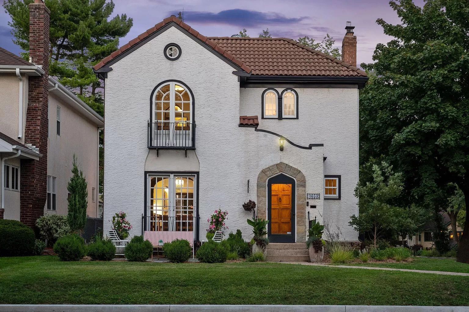 A two-story, white stucco Spanish Revival home with a terracotta tile roof, arched windows, and a small balcony.