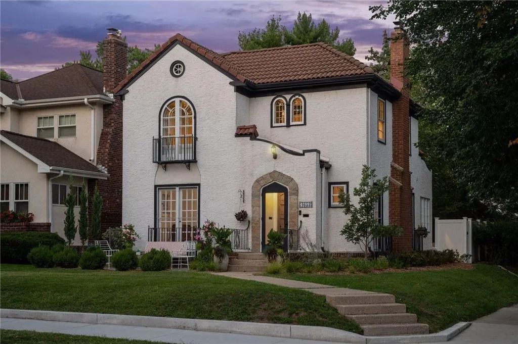 A two-story, white stucco Spanish Revival home with a terracotta tile roof, arched windows, and a landscaped front yard.