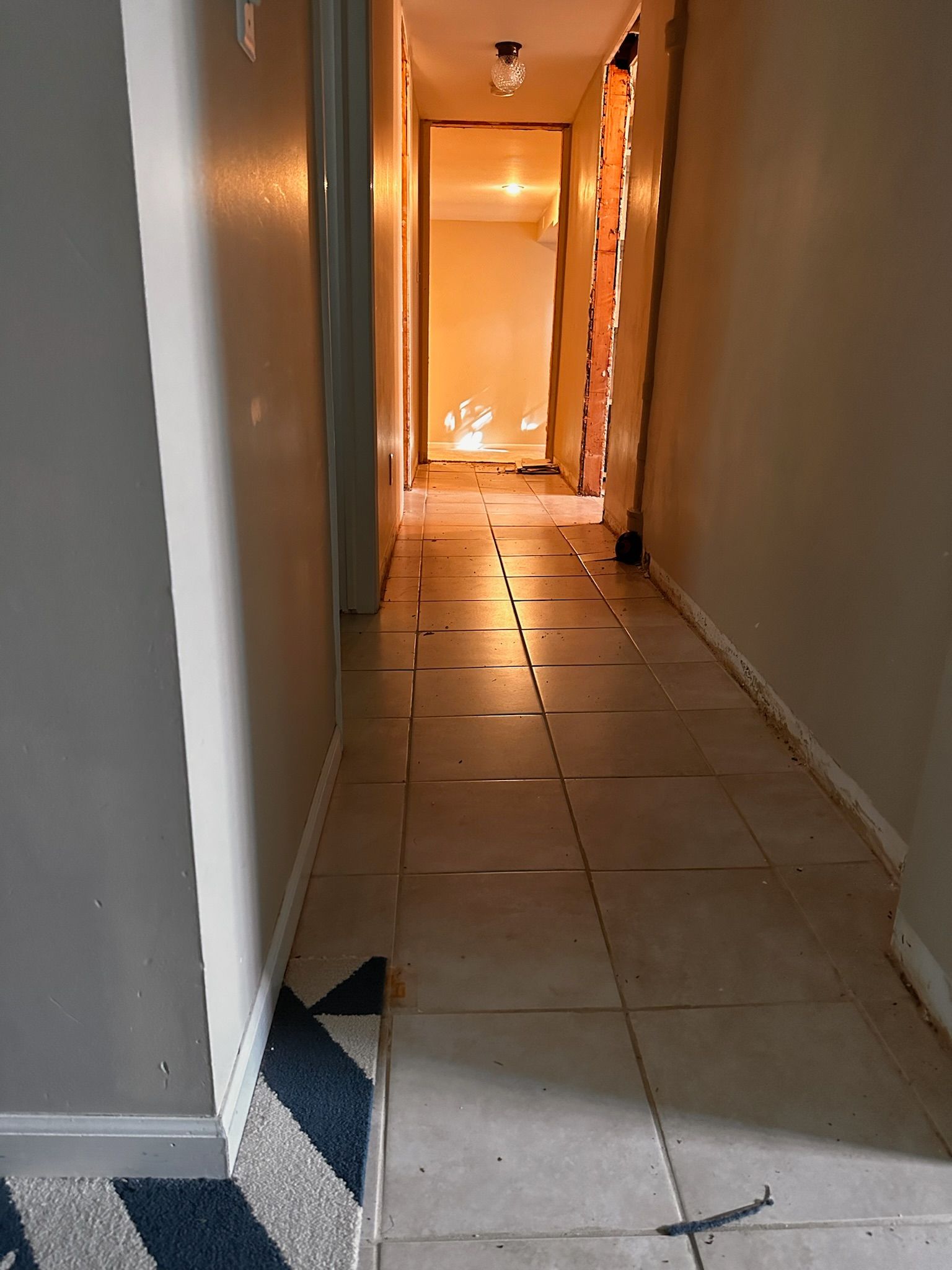A hallway with light-colored tile floors leads to an open doorway, with a partially visible room under construction beyond.