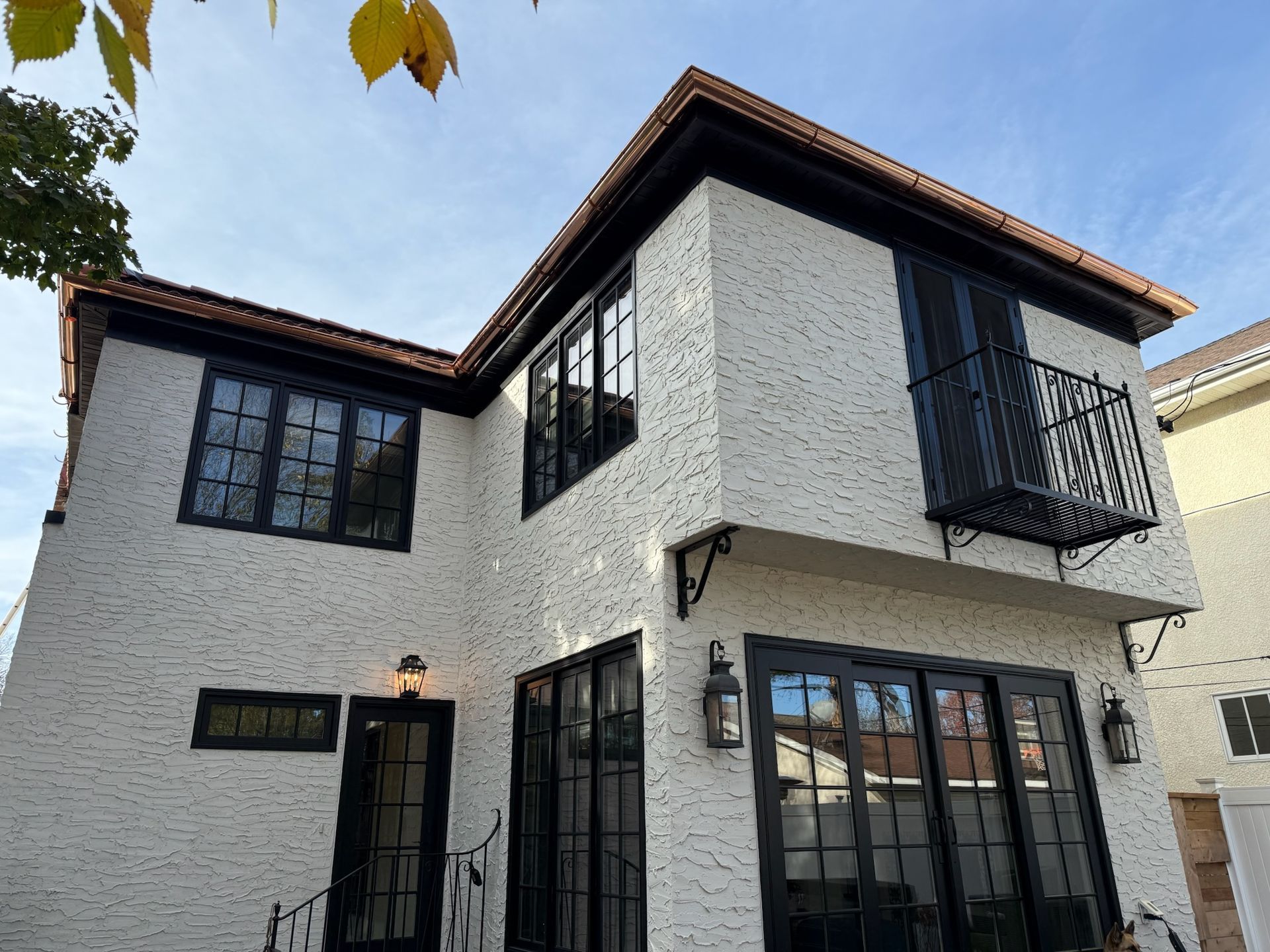 A white brick house with black windows and a balcony.