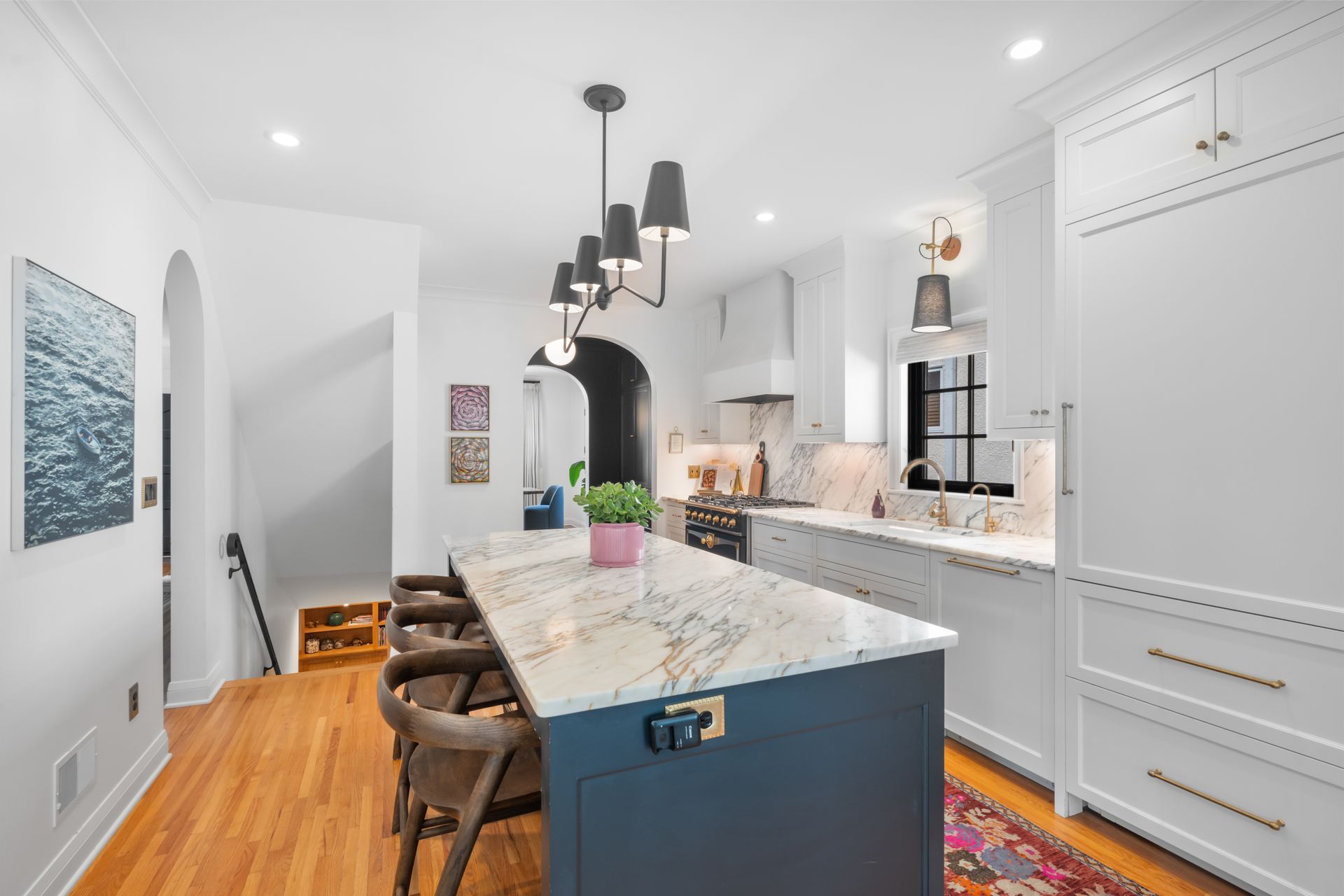 A modern kitchen featuring a dark blue island with a marble countertop, three stools, white cabinets, and pendant lights.
