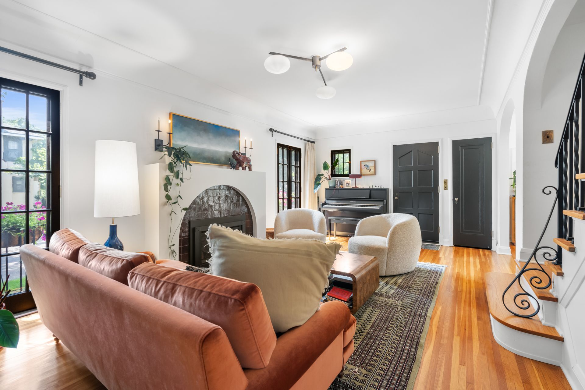 Living room with a rust-colored sofa, two armchairs, a fireplace, hardwood floors, and a piano.