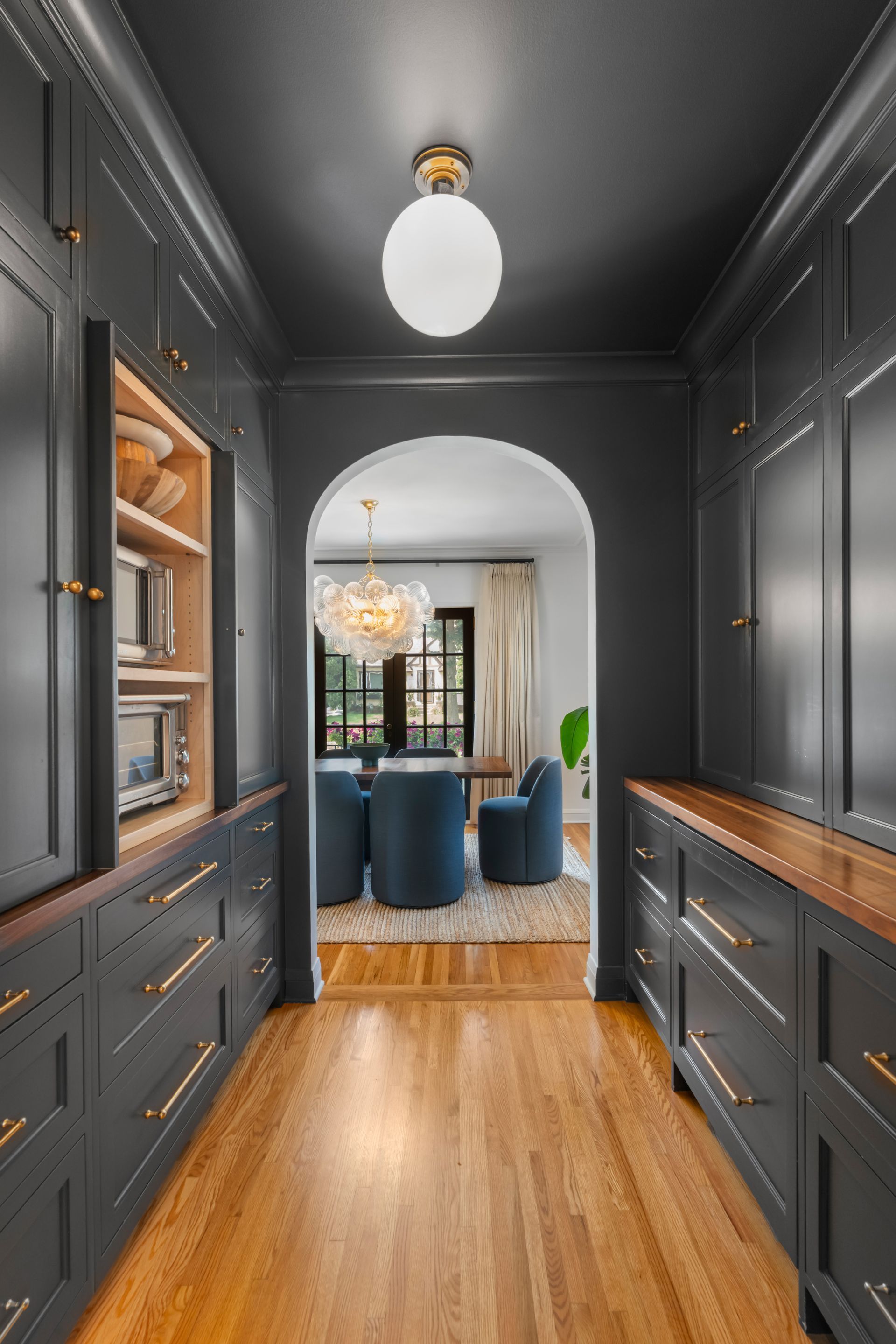 A hallway with dark grey cabinets, wood counters, and an arched doorway leading to a blue dining room.