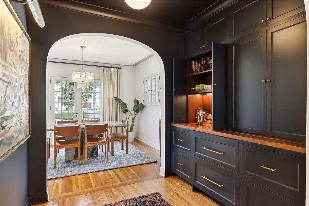 A black-walled hallway with dark cabinetry and an arched doorway looking into a dining room with a table and chairs.