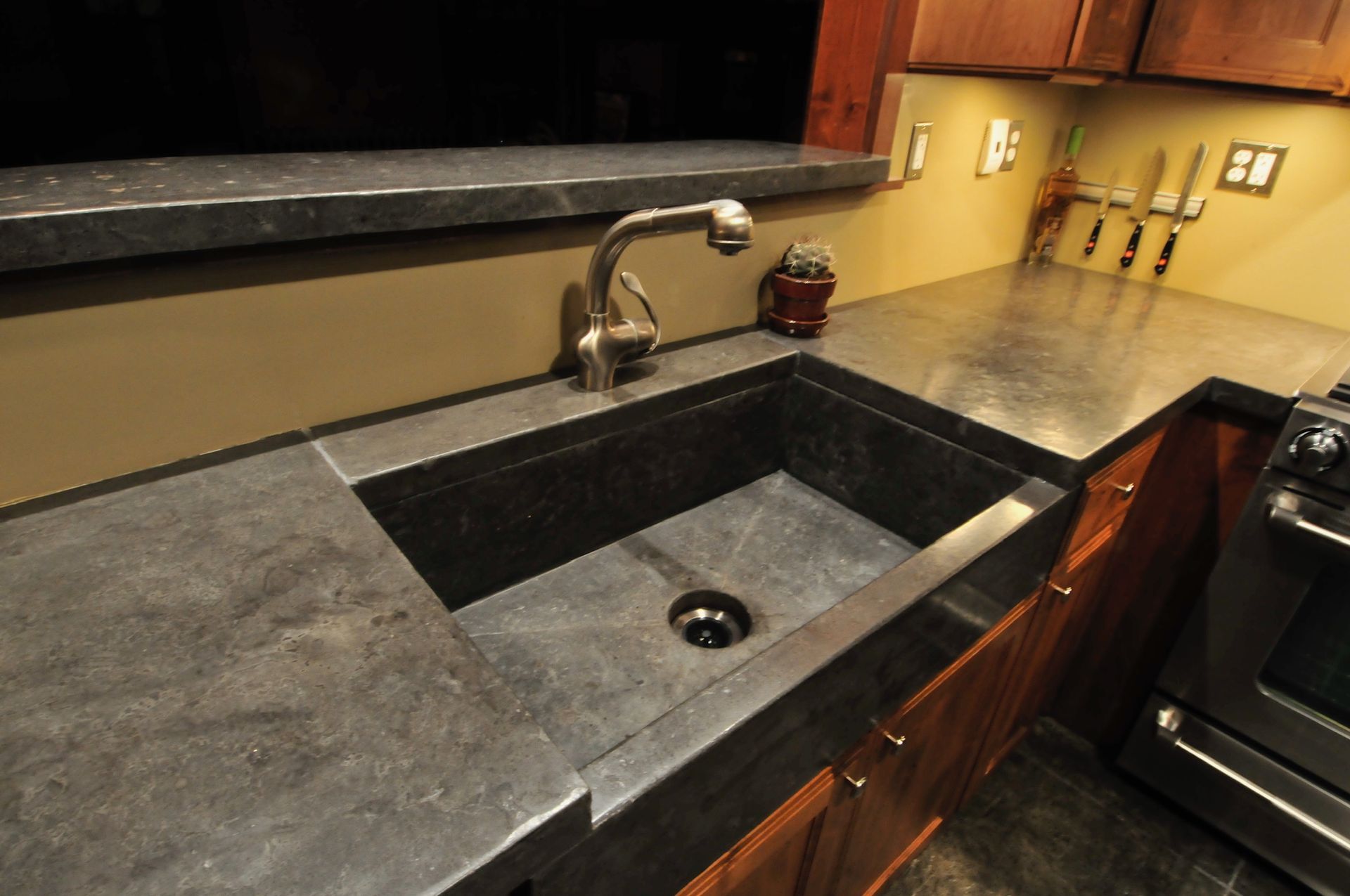 A farmhouse-style kitchen sink with dark grey stone countertops and a matching sink basin in a warm-toned kitchen.