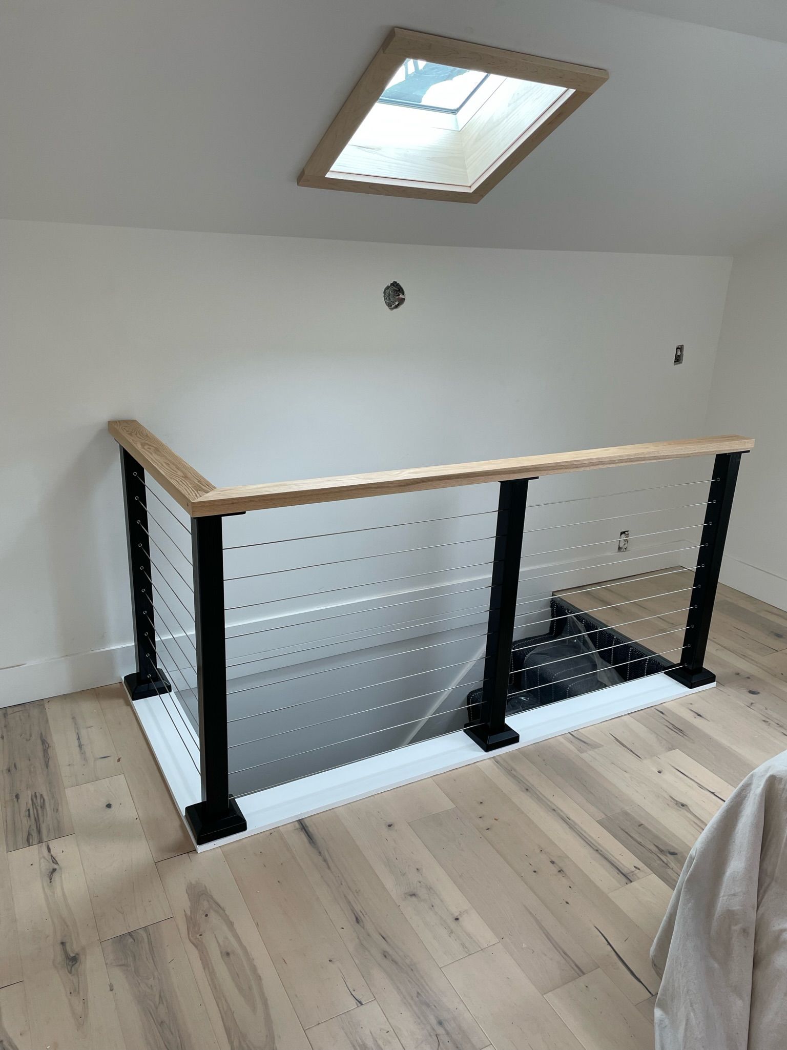 Staircase landing with black twist-style banister posts, a light wood handrail, and clear glass panels under a skylight.