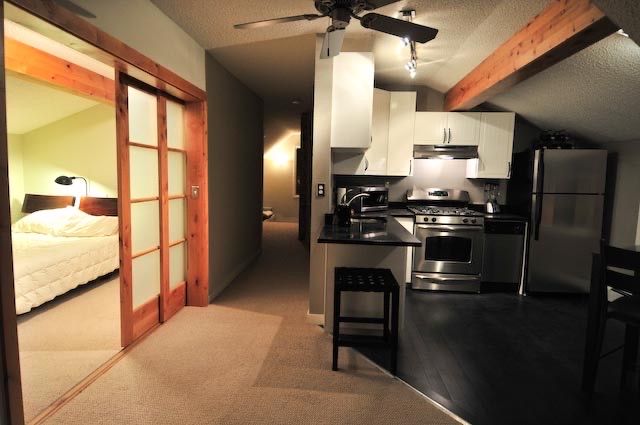 A wide-angle view of a modern loft apartment featuring a kitchen with stainless steel appliances and a sliding bedroom door.