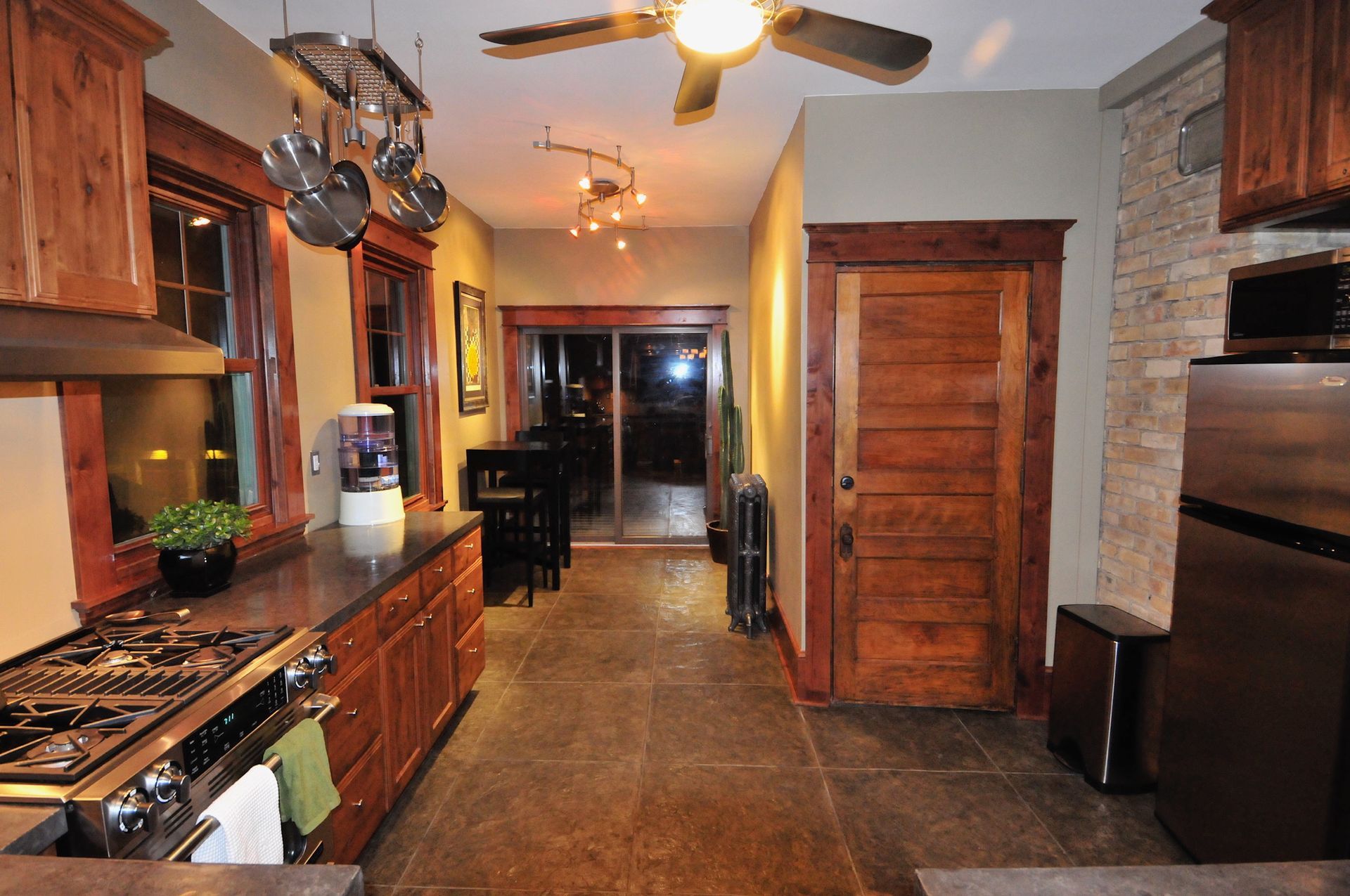 A rustic-style kitchen featuring wood cabinetry, stone flooring, stainless steel appliances, and a wooden interior door.