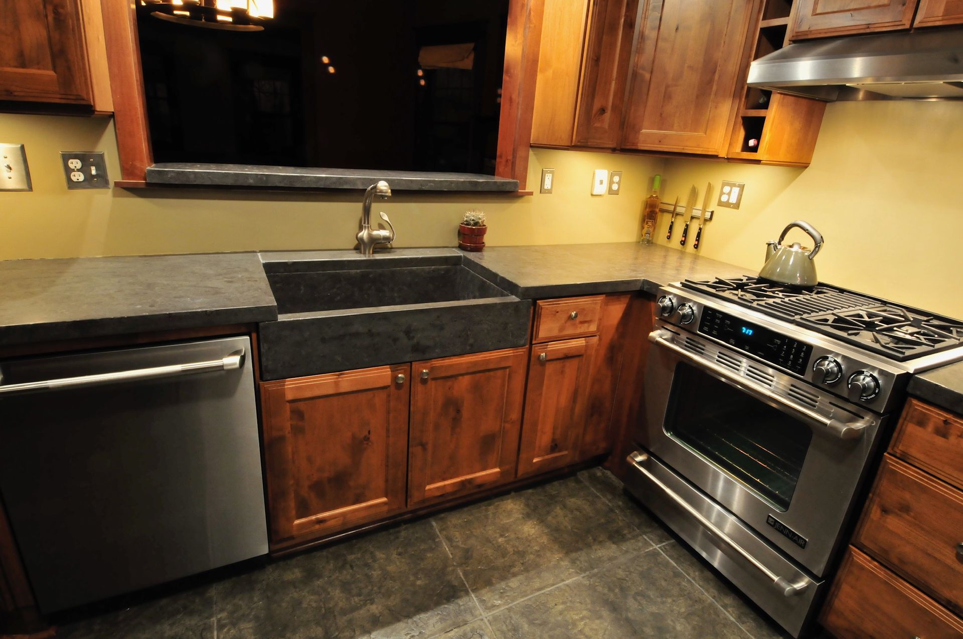 A kitchen interior featuring a farmhouse sink, stainless steel dishwasher and gas range, and warm wood cabinetry.