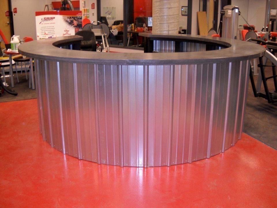 A curved bar with a dark countertop and metallic, corrugated siding, situated in a room with a bright red floor.
