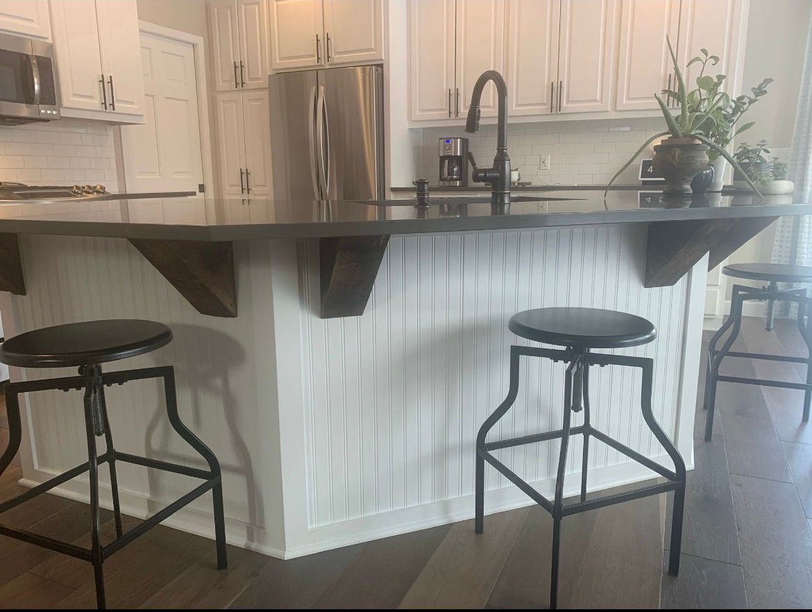 A kitchen island with a dark countertop and white vertical-plank base, featuring three black industrial-style bar stools.