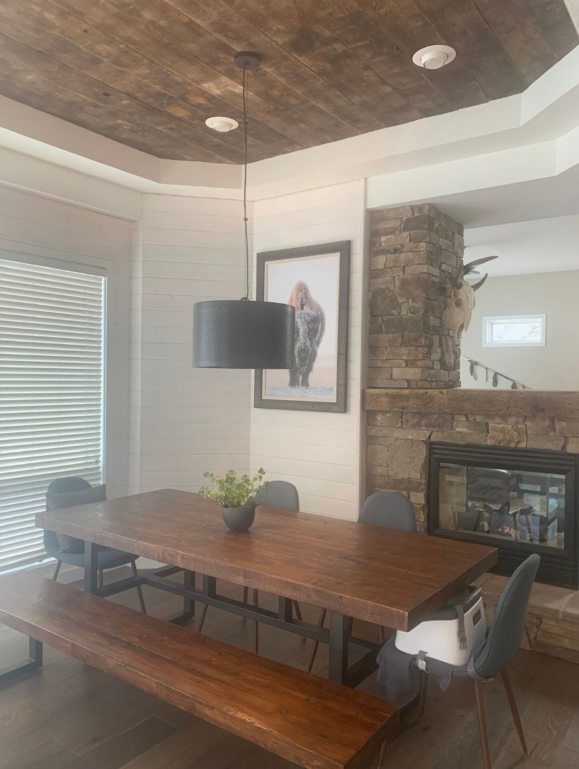 A rustic dining area with a wooden table, a long bench, and a modern pendant light beneath a coffered wood-plank ceiling.