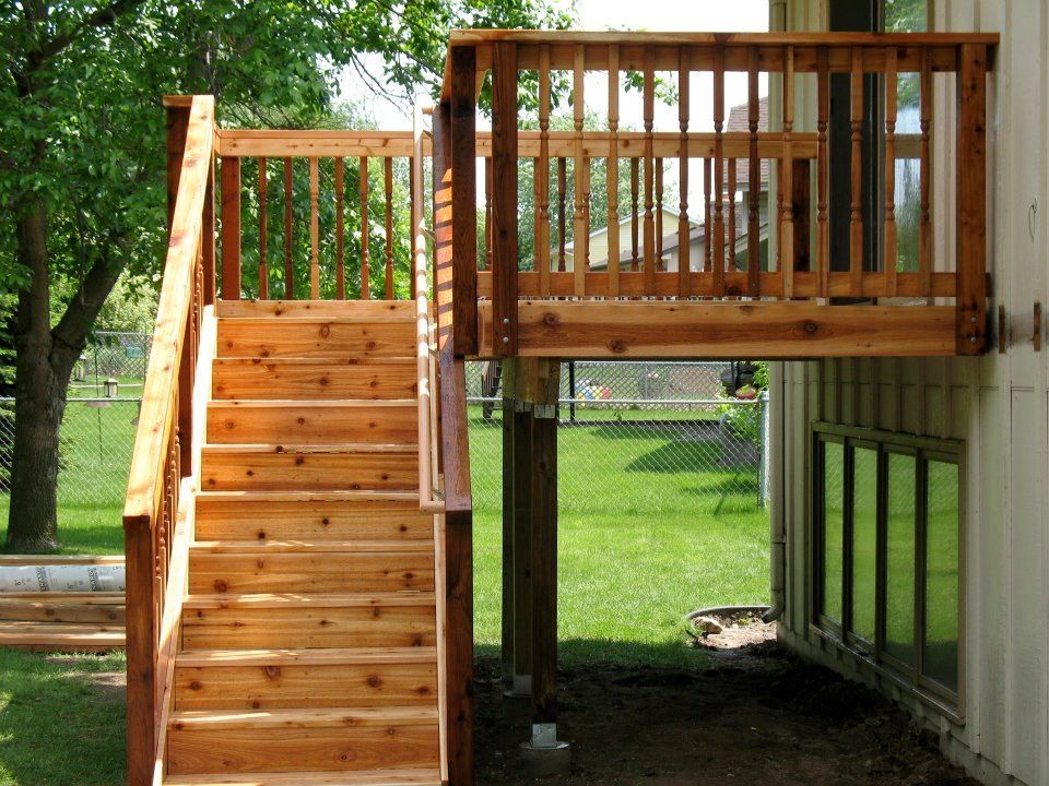 A wooden deck attached to the side of a house, featuring a short staircase leading down to a grassy yard.