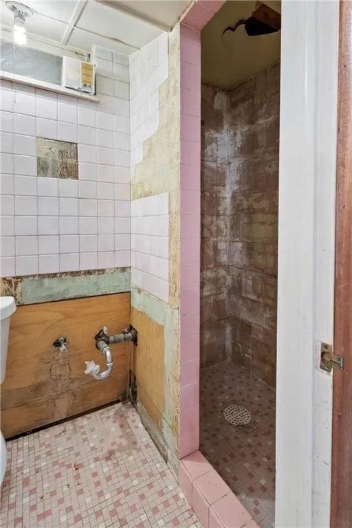 A bathroom under renovation with exposed wood walls, unfinished tile, and an open, tiled shower stall.
