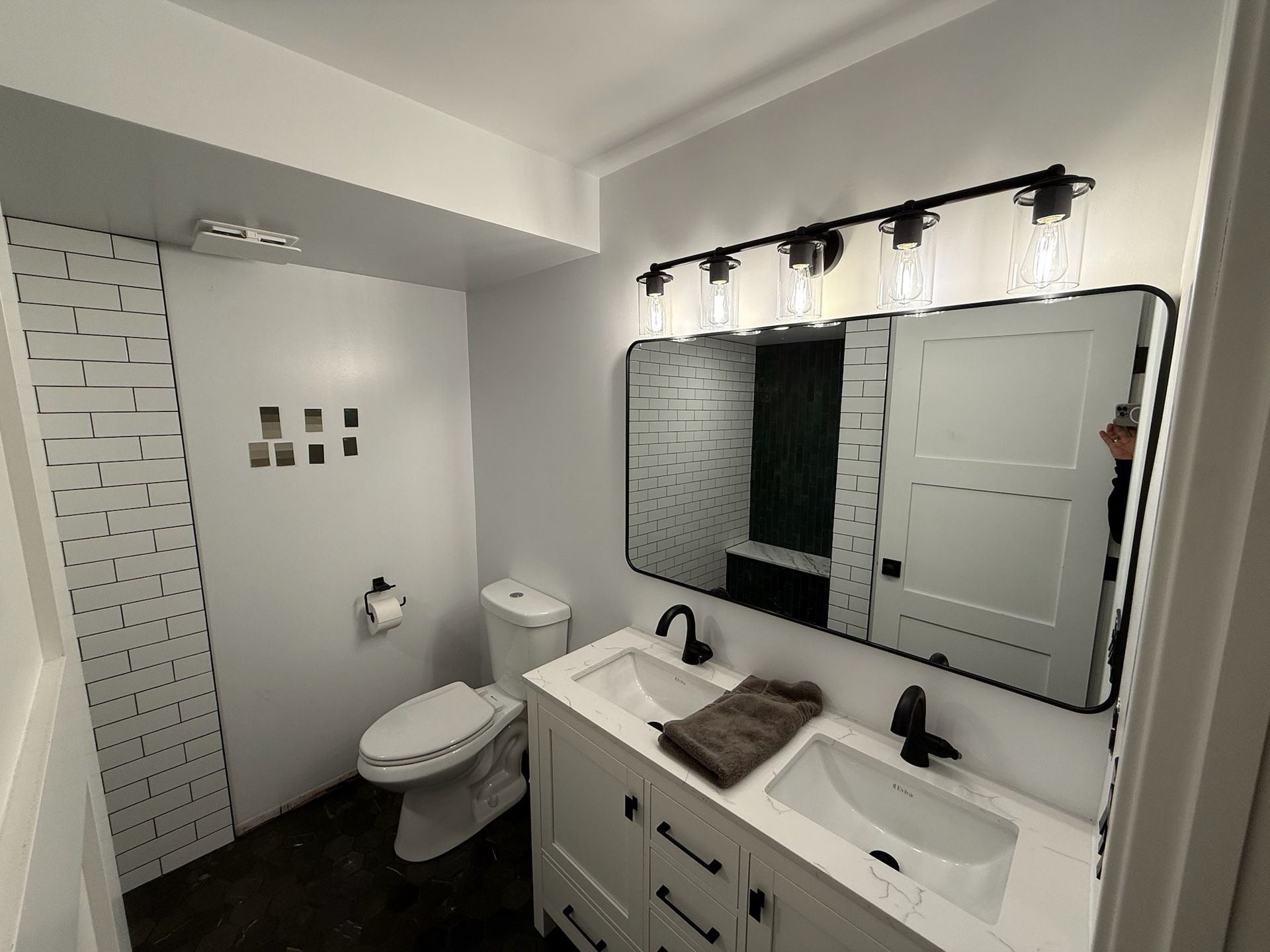 A modern bathroom with a double vanity, a large rectangular mirror, black fixtures, and a white brick accent wall.