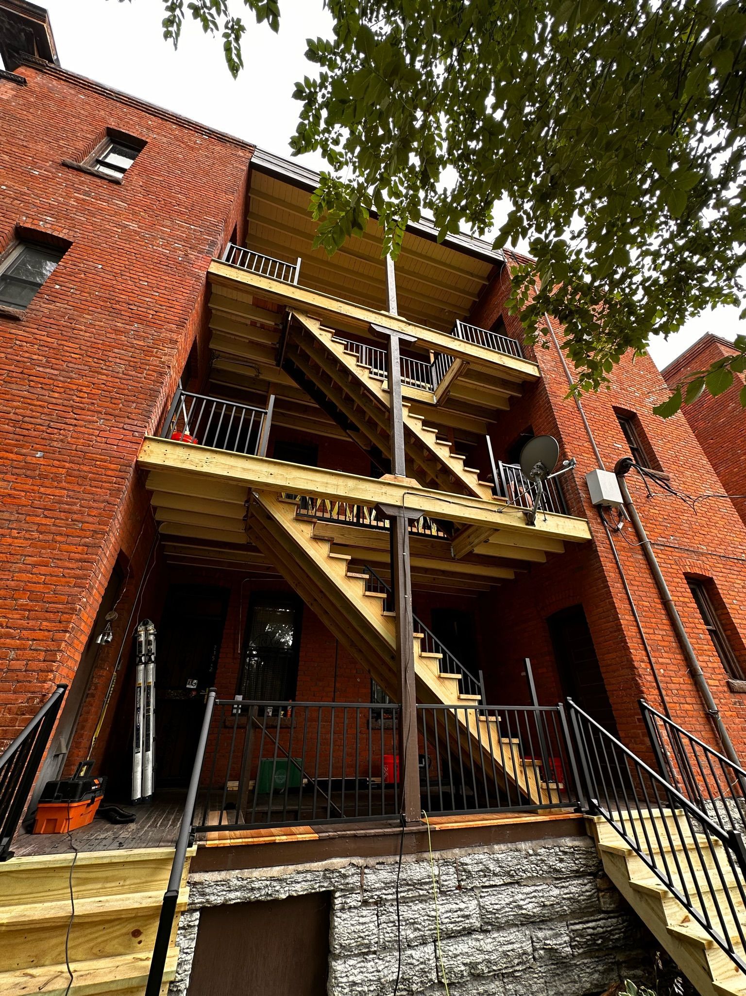 A low-angle view of a red brick apartment building with newly constructed wooden balconies and external staircases.