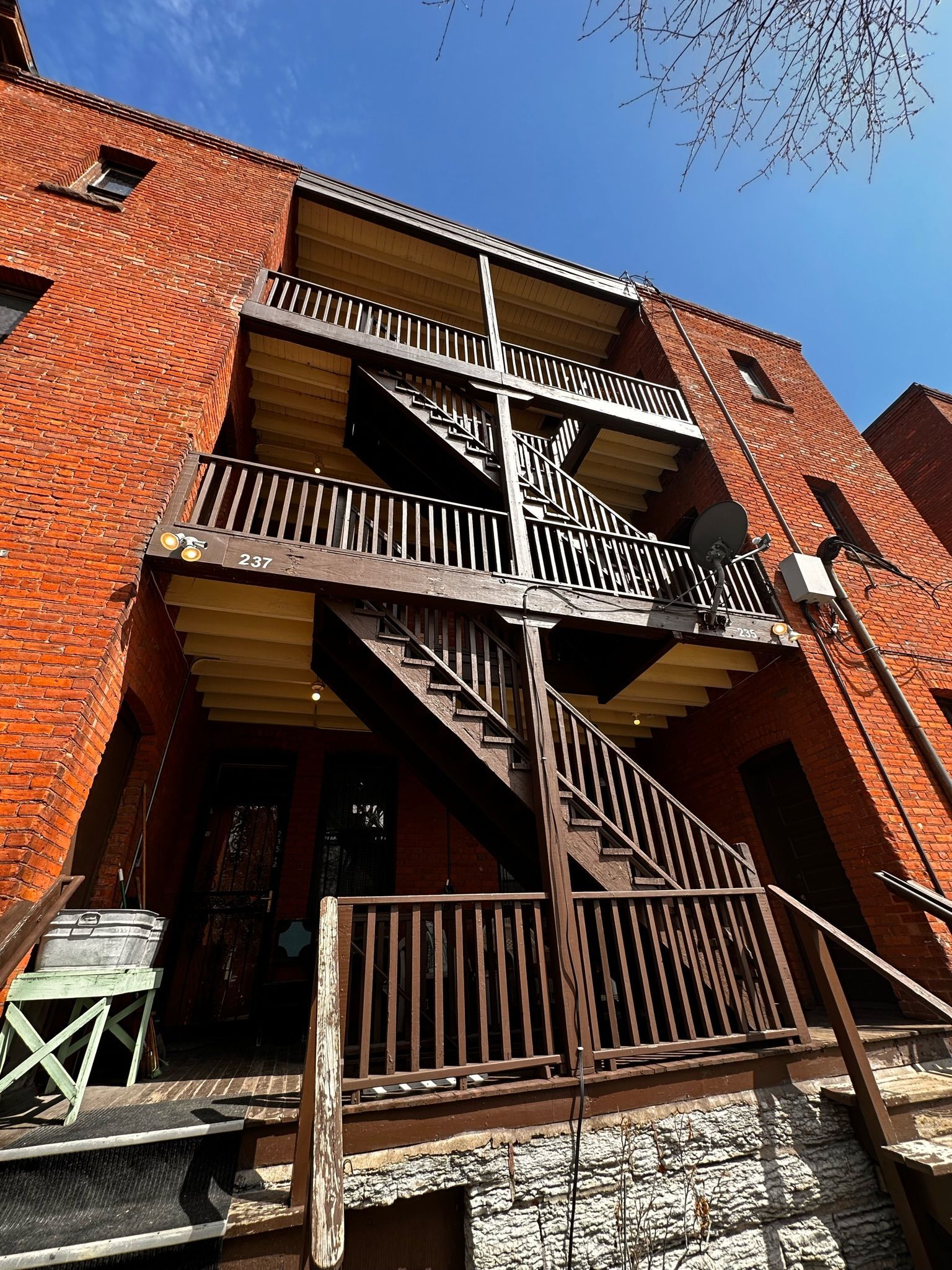 A low-angle view of a red brick building with an exterior wooden staircase and balconies leading up to the top floor.