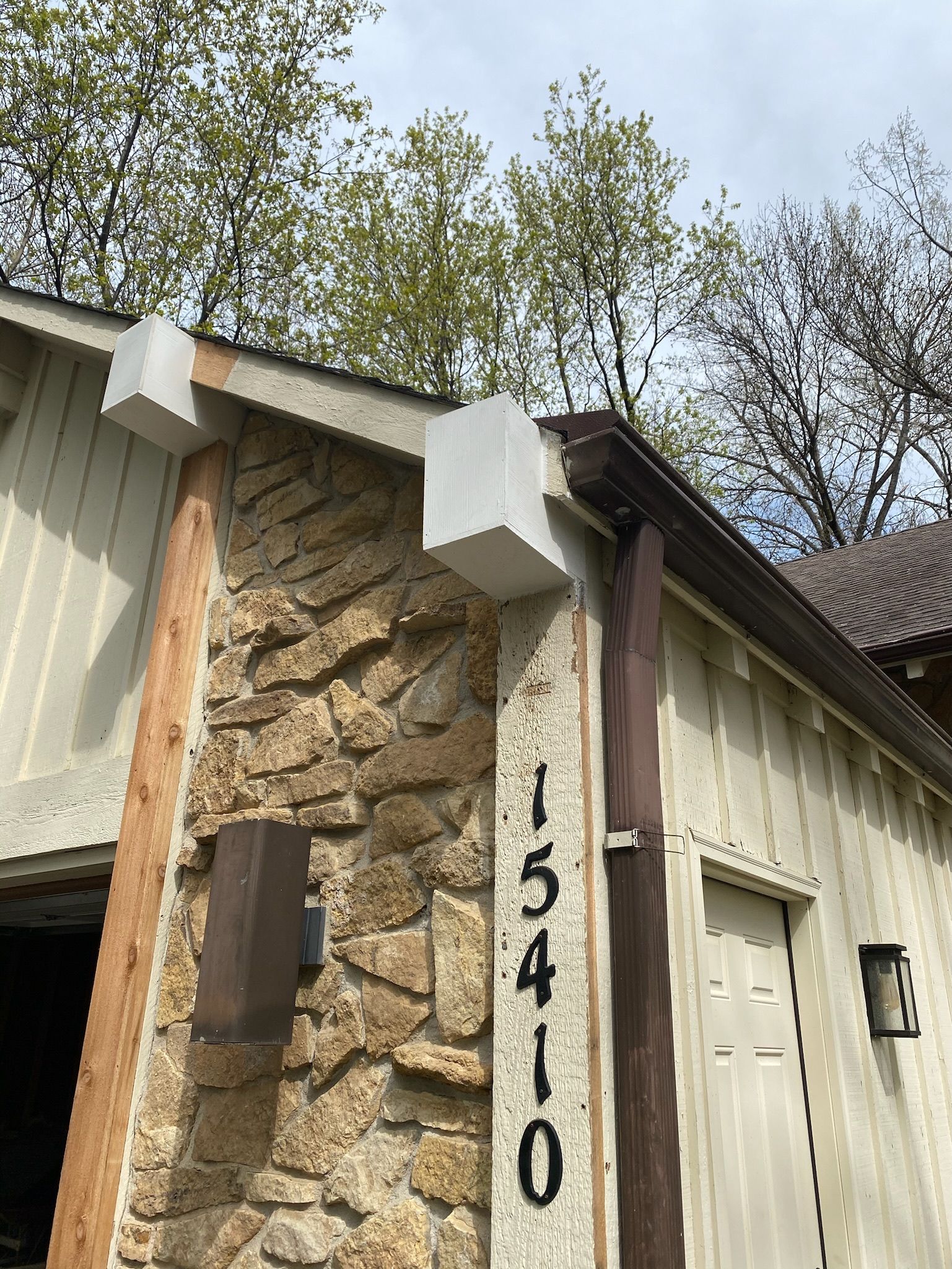 The house number 15410 displayed vertically on a stone wall exterior near the roofline and trees.