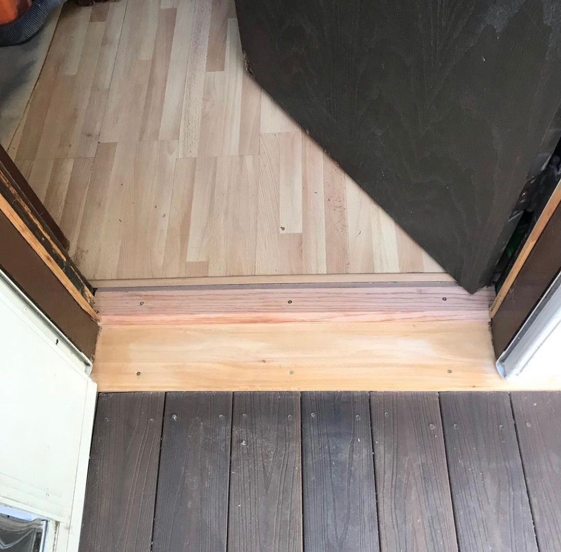 An open doorway transition between a dark wooden deck outside and a light wood-look interior floor.