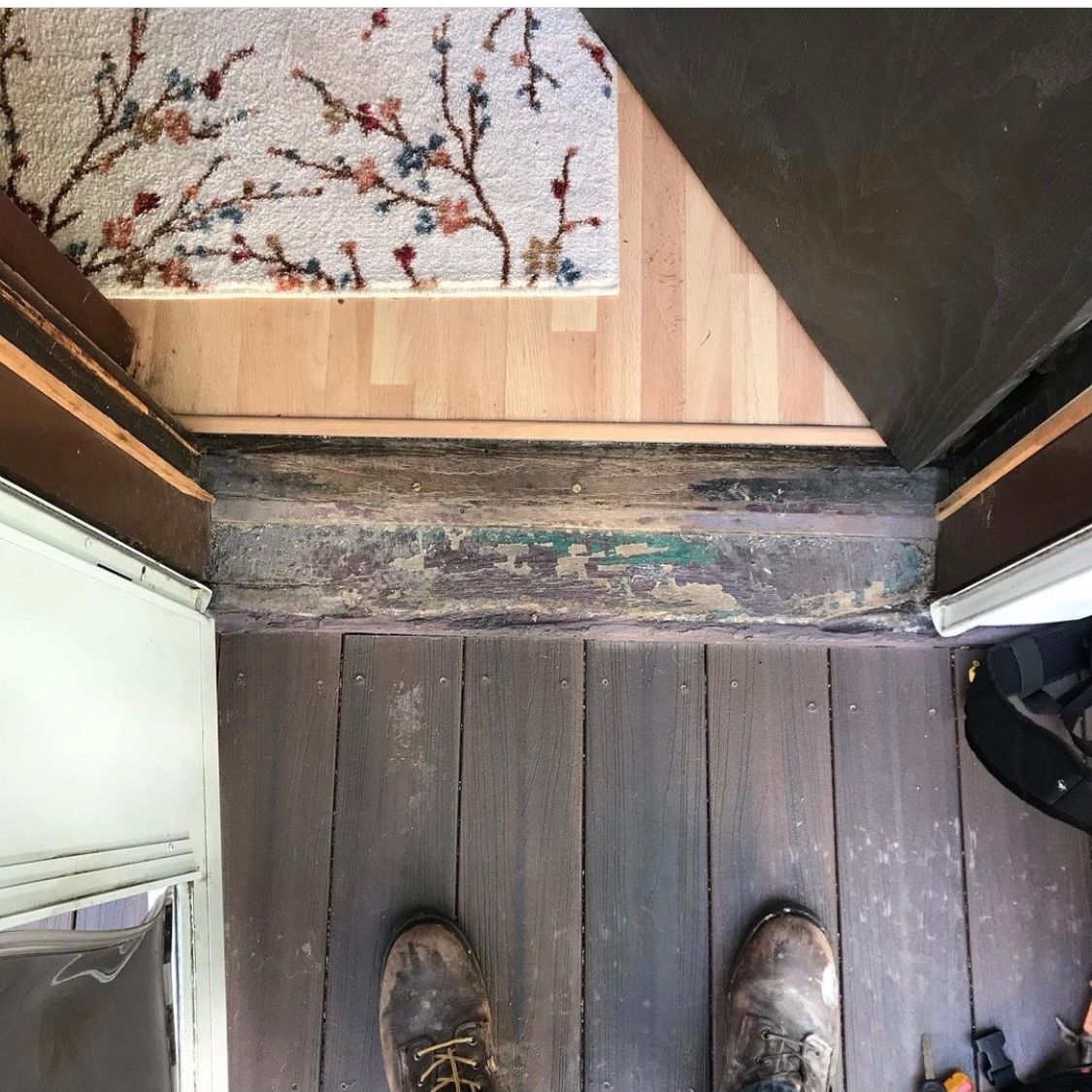 A first-person view looking down at a worn, weathered threshold between an outdoor porch and indoor wood flooring.