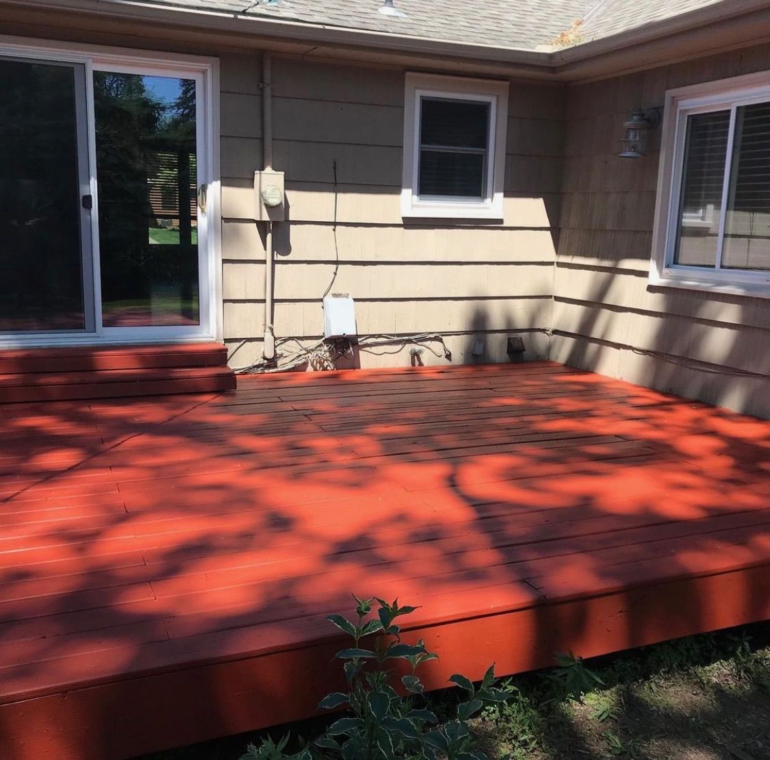 A freshly painted terracotta-colored wooden deck attached to the back of a beige house with a sliding glass door.