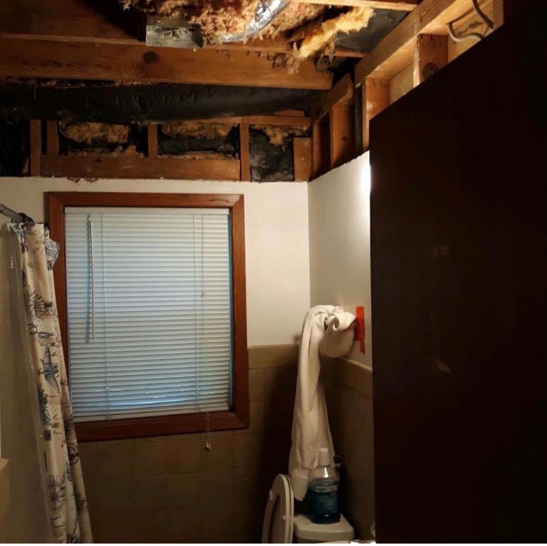 Bathroom with an exposed wooden ceiling frame and insulation above a window, a white towel, and a toilet.