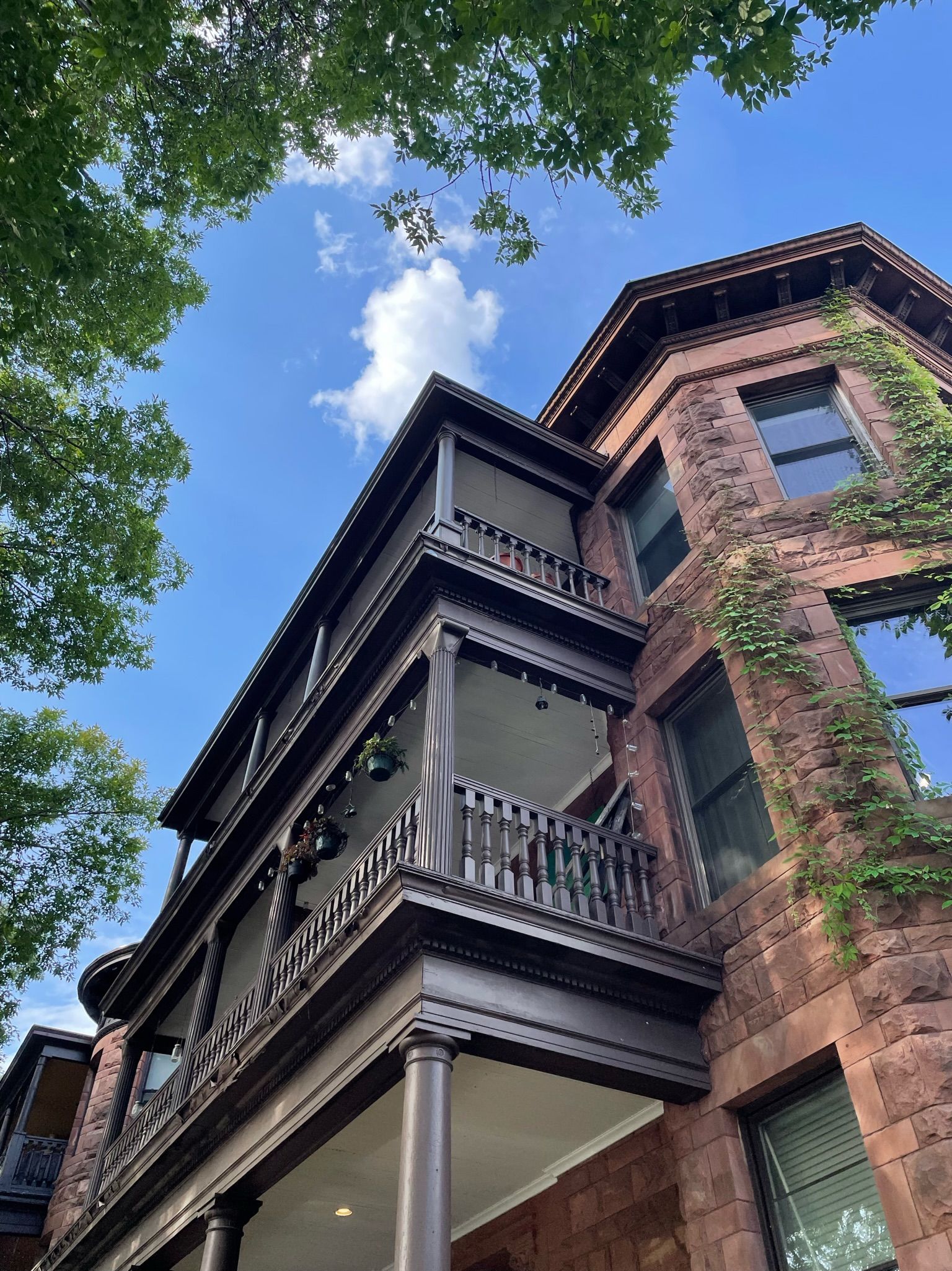 Low-angle view of a multi-story brownstone building with tiered, decorative dark wood balconies under a blue sky.