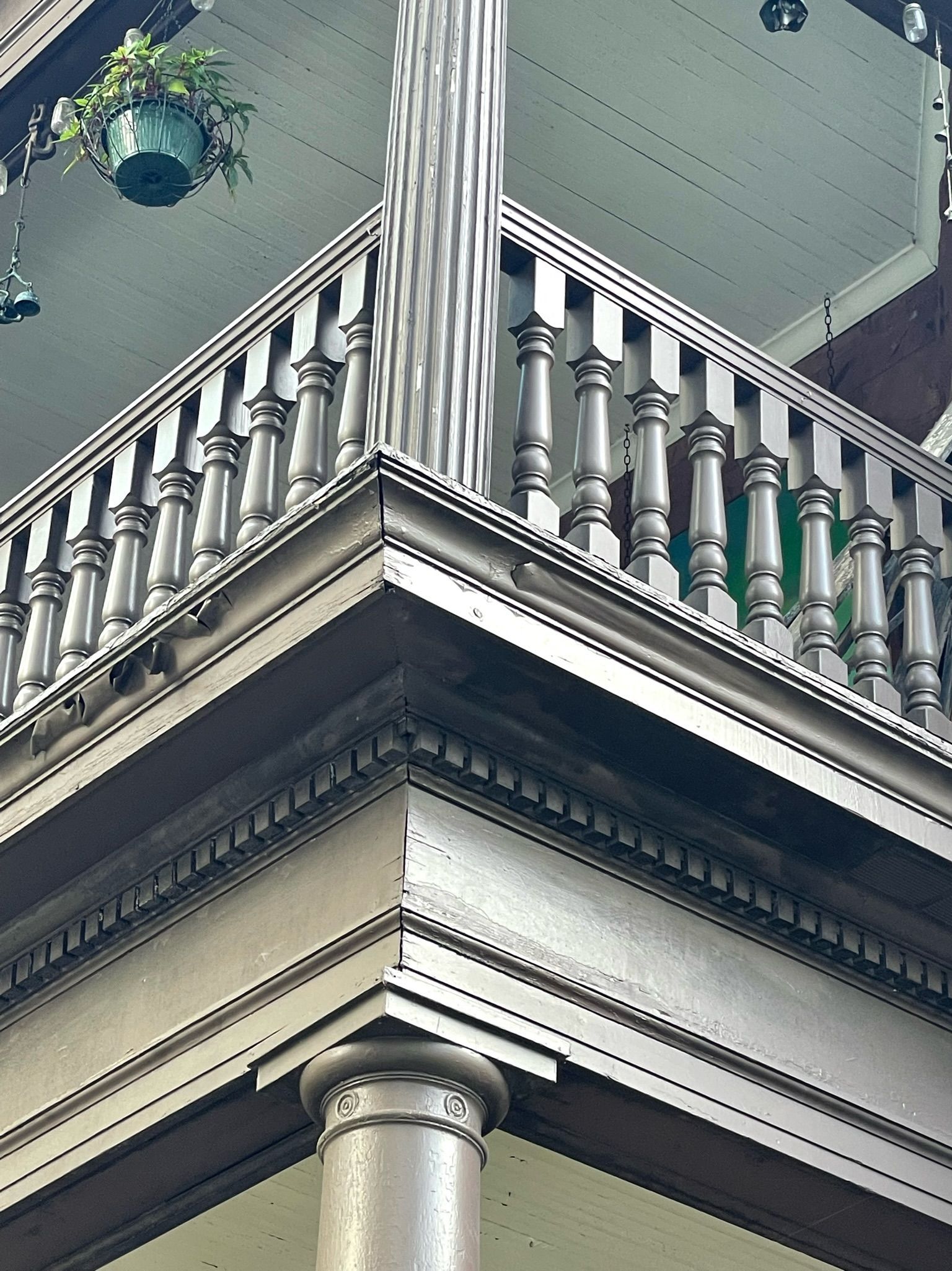 A low-angle view of a building corner featuring a light-colored wooden porch railing with balusters and a potted plant.