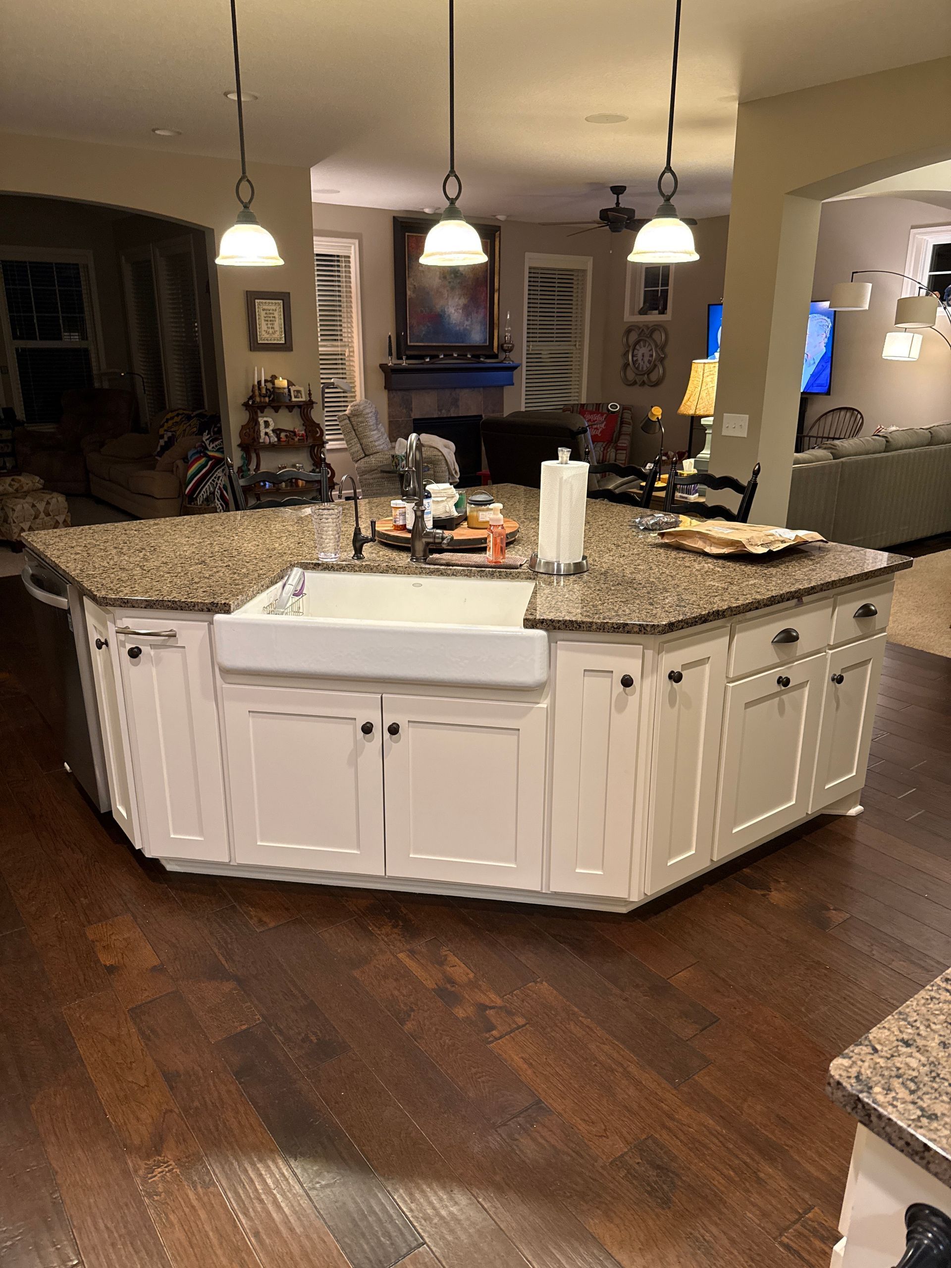A cream-colored, multi-sided kitchen island with a farmhouse sink, granite countertop, and three hanging pendant lights.