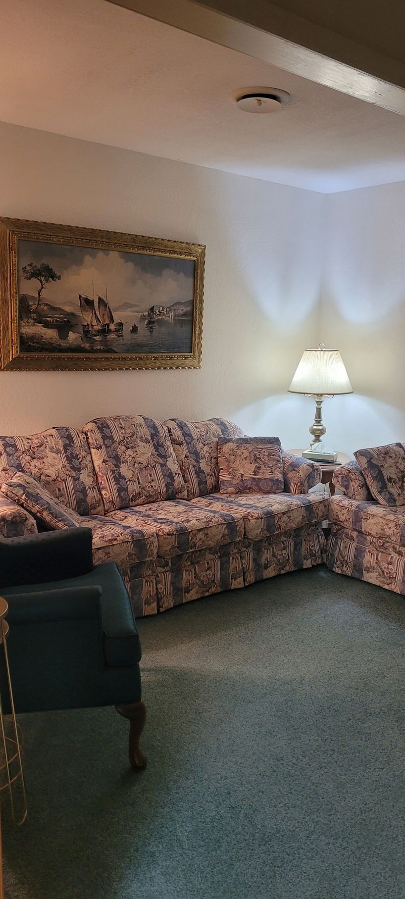 A living room with a couch , chair , lamp and painting on the wall.
