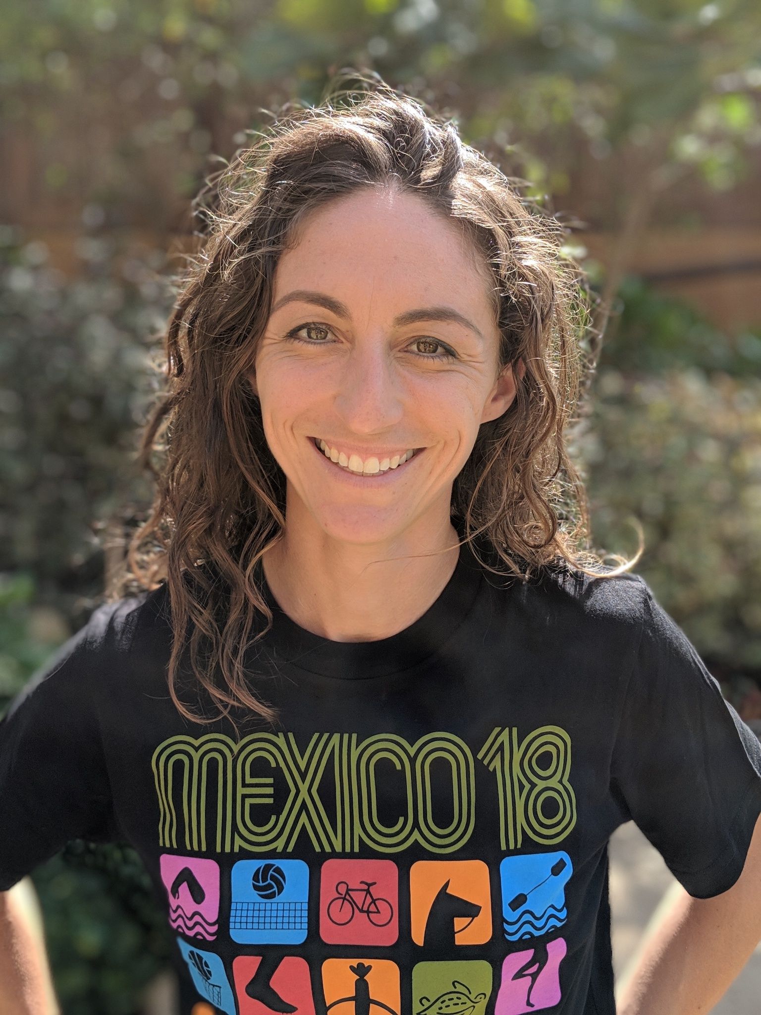 Smiling person outdoors wearing a black T-shirt with colorful “Mexico” graphics.