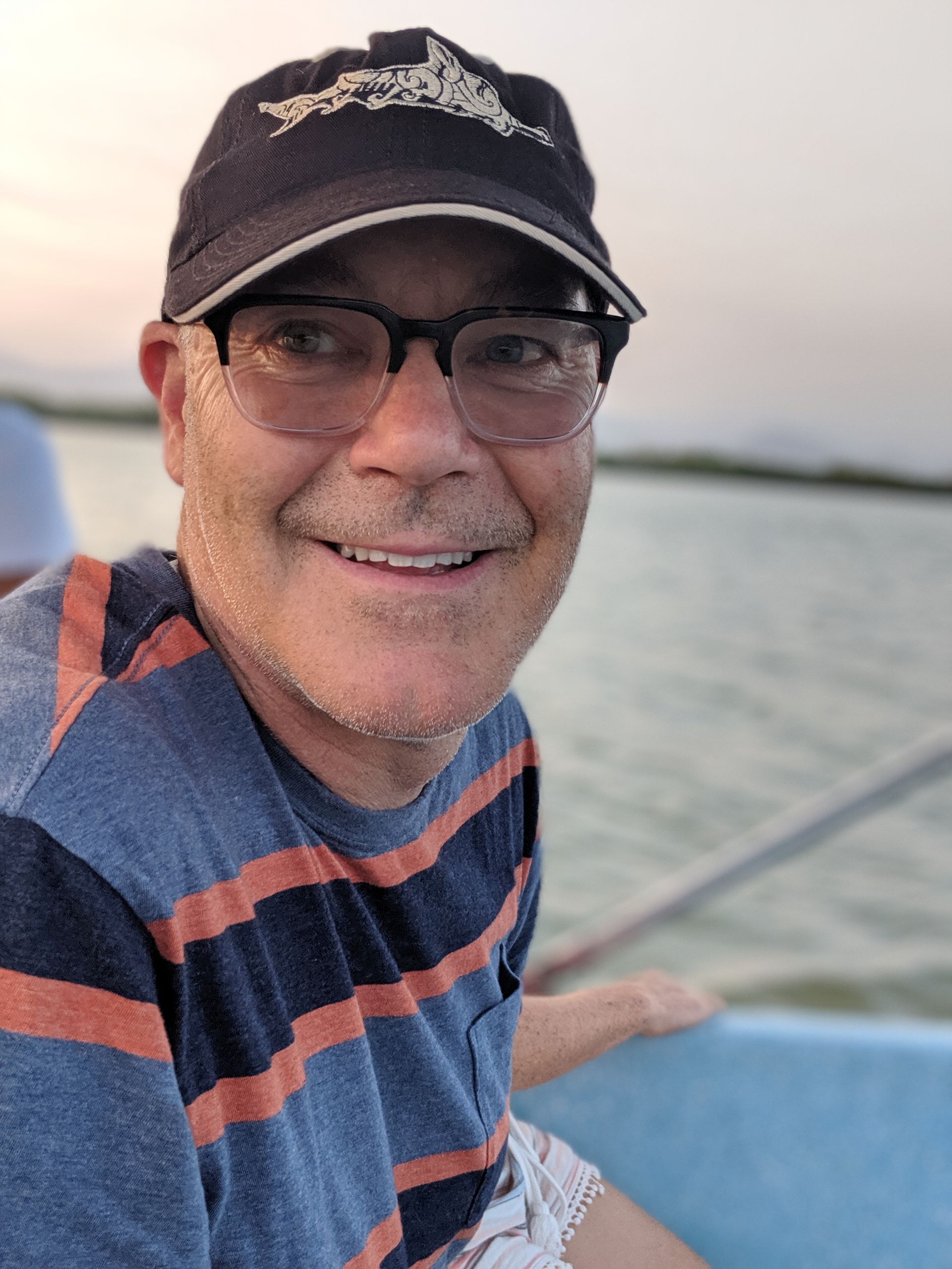 Smiling person in a black cap and glasses on a boat at sunset