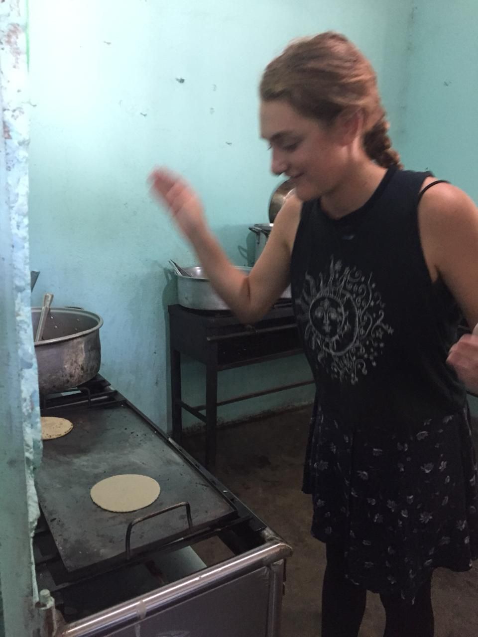 Woman smiling while cooking flatbread on a stovetop in a small kitchen