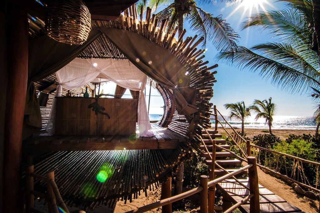 Tropical beach hut with thatched roof, wooden stairs, and ocean view under bright sun