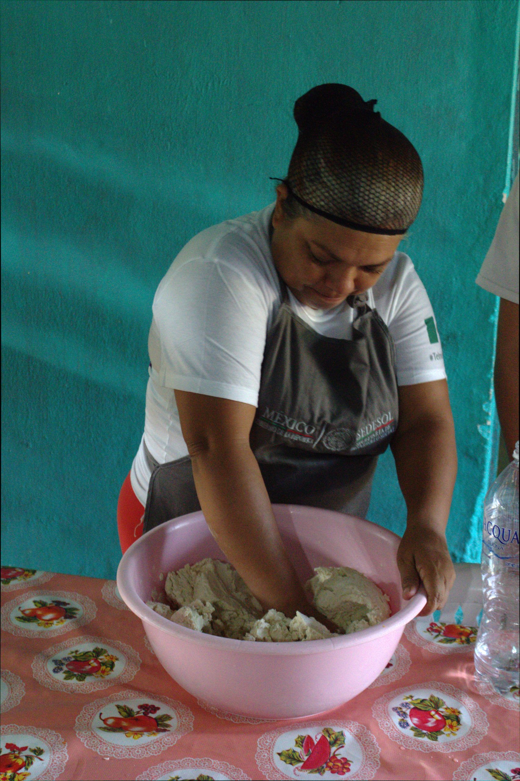 Person kneading dough in a pink bowl on a patterned table indoors