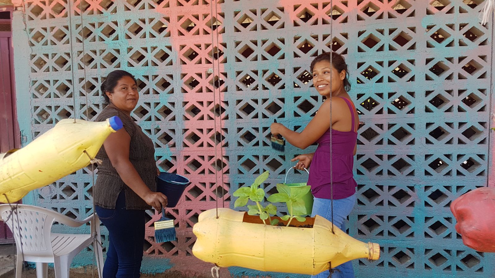 Two people smiling beside hanging yellow produce bags in front of a colorful lattice wall.