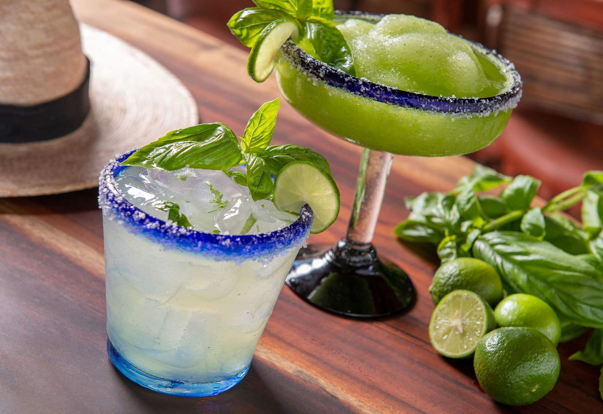 Two lime cocktails in blue-rimmed glasses on a wooden tray with fresh mint and limes
