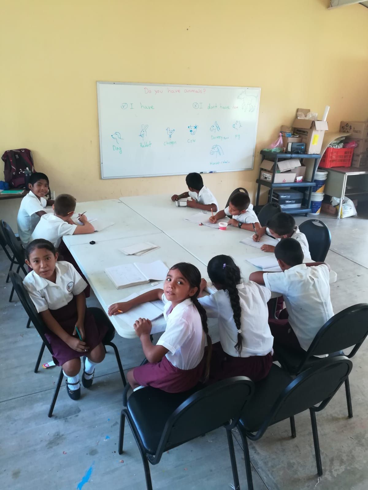 Students seated around a large table in a classroom, working together near a whiteboard.