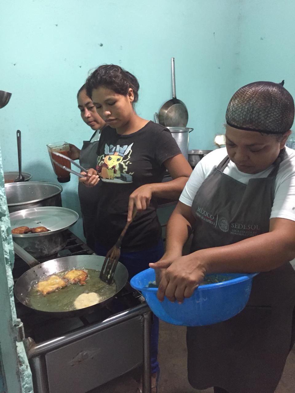 Two people cooking in a kitchen, stirring food in a large pan and straining ingredients in a blue bowl.