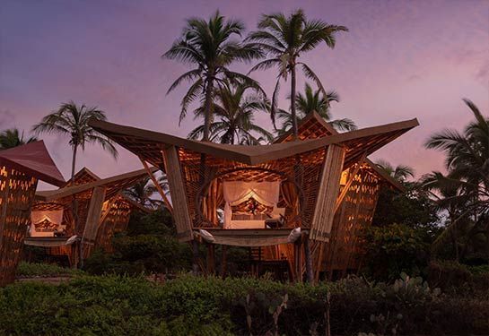 Tropical resort villas lit warmly at dusk, with palm trees and a pink-purple sky