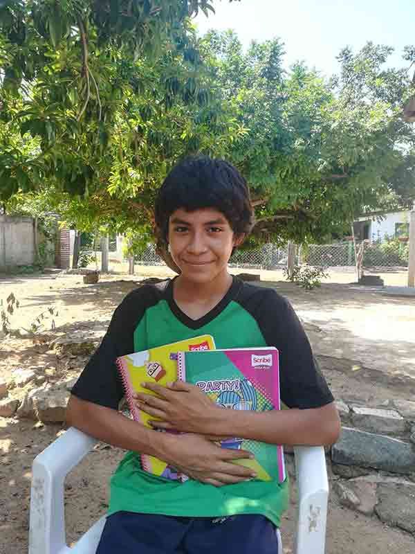 Person sitting outdoors on a white chair, holding colorful notebooks under trees.