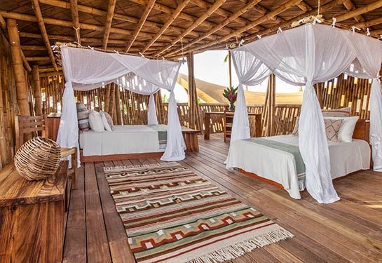 Open-air wooden bungalow with two white-canopy beds and woven decor