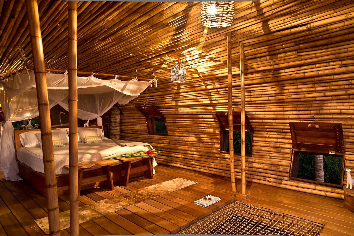 Rustic bamboo bedroom with a bed, woven walls, hanging lights, and a small window