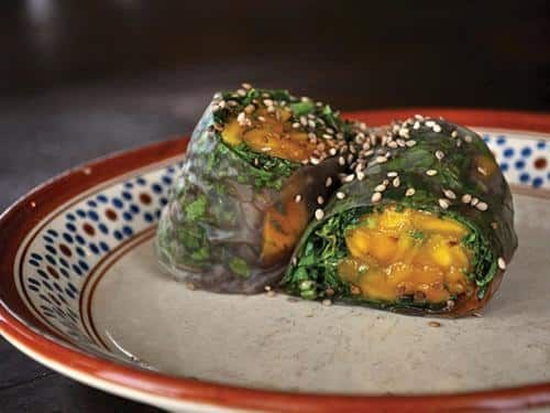 Two green vegetable sushi rolls with orange filling on a patterned plate