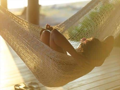 Person relaxing in a woven hammock on a sunlit wooden deck