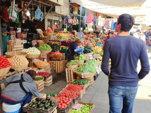Bustling outdoor market with colorful produce stalls and shoppers in a narrow aisle